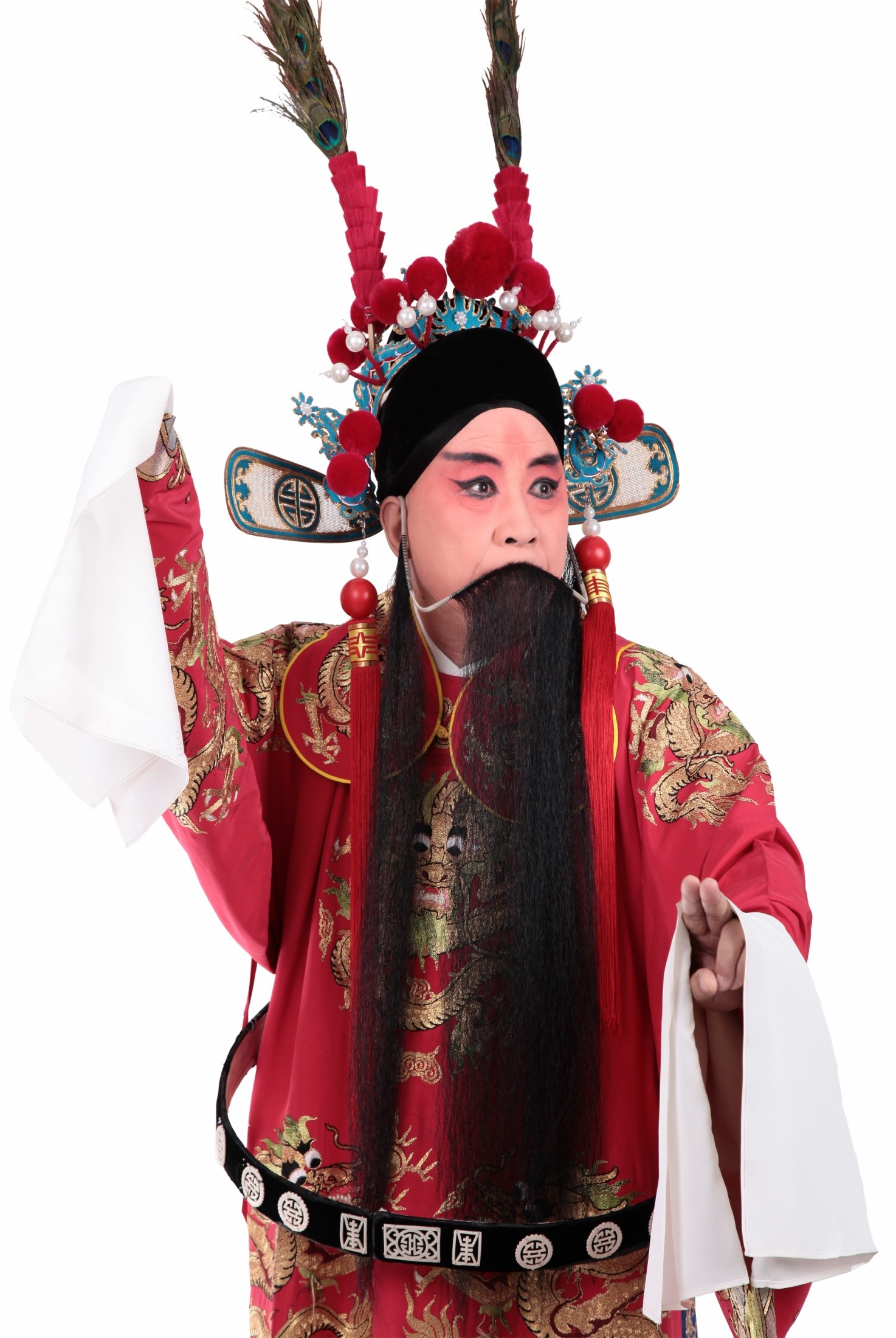 在那纯白的背景前，身穿红色戏服的他，头戴华丽帽饰，仿佛从历史的长河中走来，带着岁月的痕迹和故事。他站在那里，就像一座山，稳重而不可动摇。他的每一个动作，每一个表情，都充满了力量，让人感受到京剧艺术的魅力。他的眼神中透露出一种深邃与思考，思索着人生的大道理。